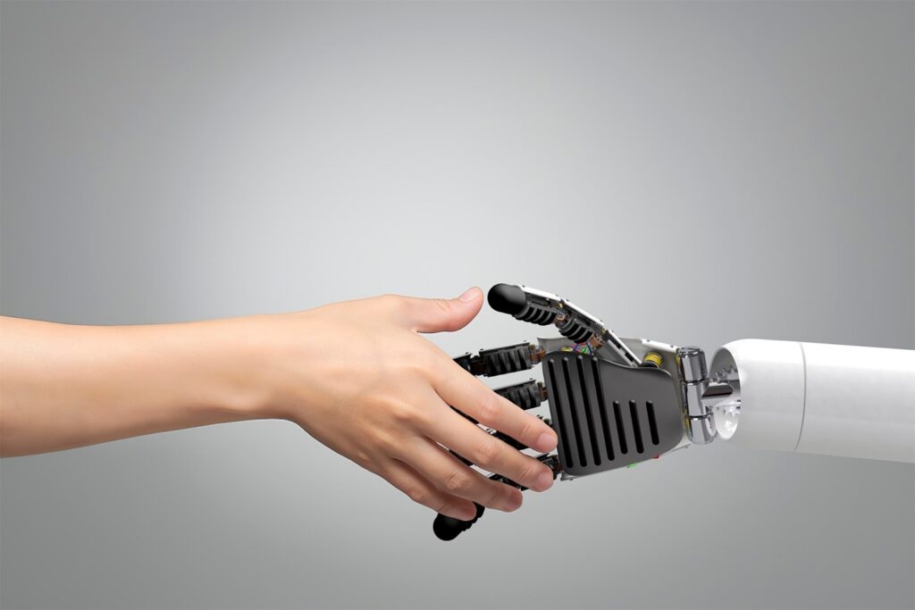 A human hand and a robotic hand reach out to shake hands against a plain gray background, symbolizing the connection between humans and technology—much like using ChatGPT prompts for higher education marketing enhances collaboration and innovation.